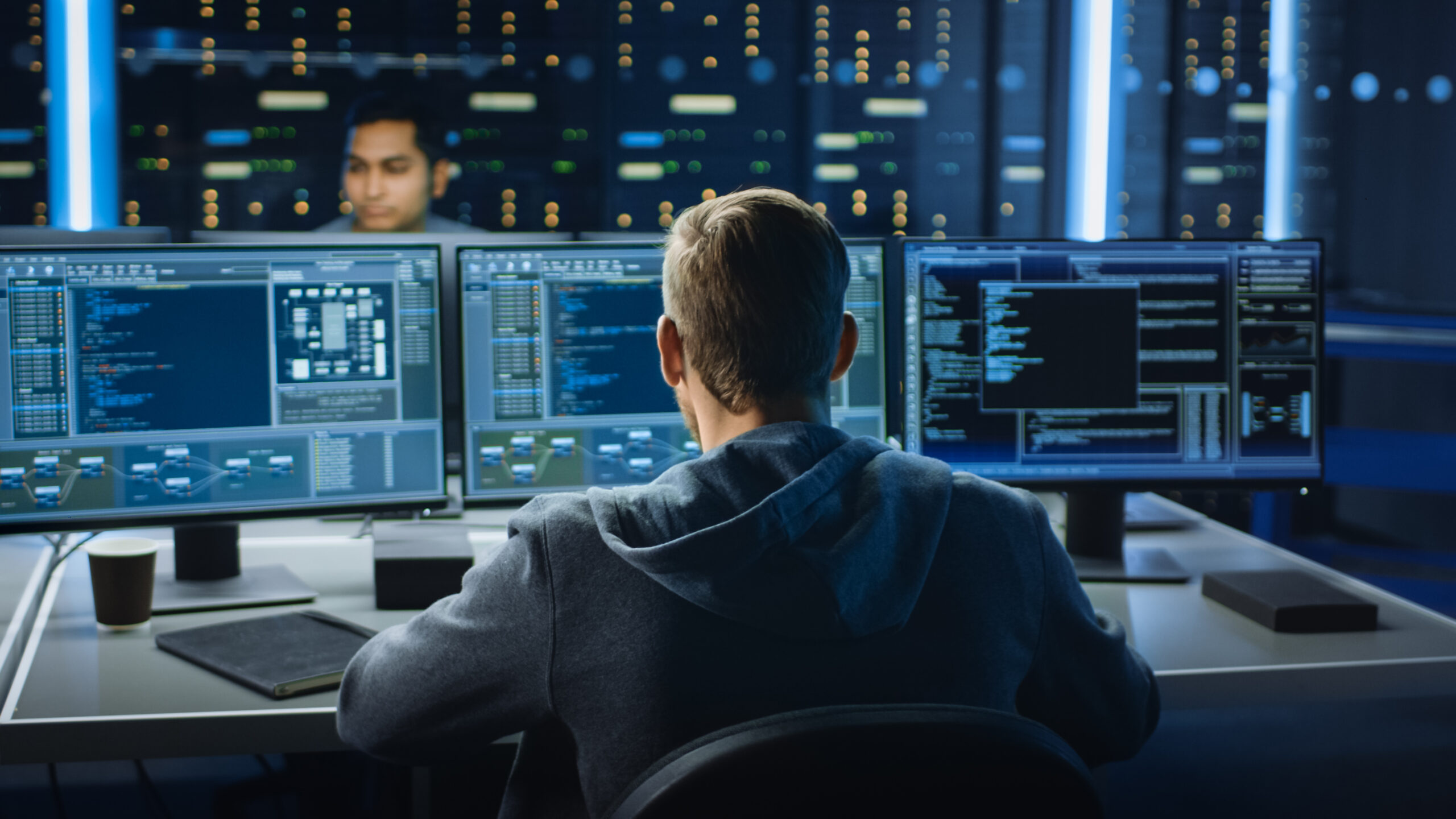 IT Specialist Works on Personal Computer with Screens Showing Software Program with Coding Language Interface. In the Background Technical Room of Data Center with Professional Working